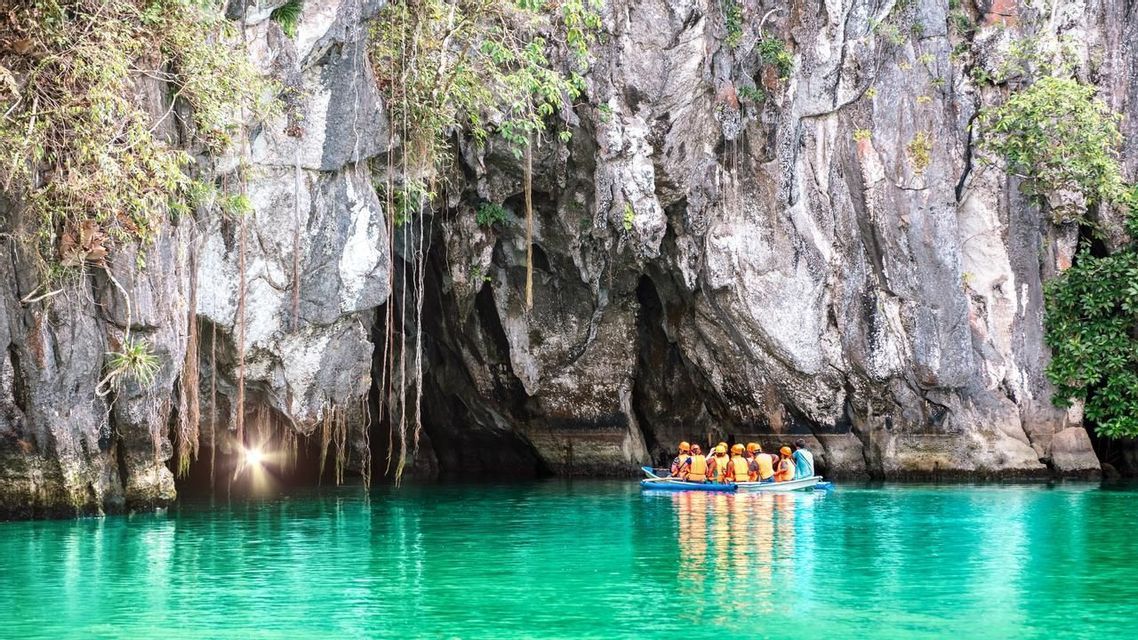 A WeRoad group trip on a boat approaches a large sea cave with turquoise water and a light shining from the entrance.