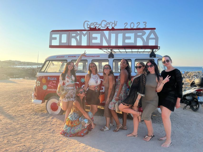 Un viaje en grupo de WeRoad de mujeres posando para una foto frente a una furgoneta vintage roja y blanca en una playa al atardecer.