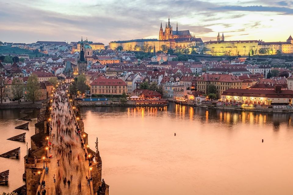 Prague Castle and St Vitus Cathedral glowing above the Vltava river at sunset.