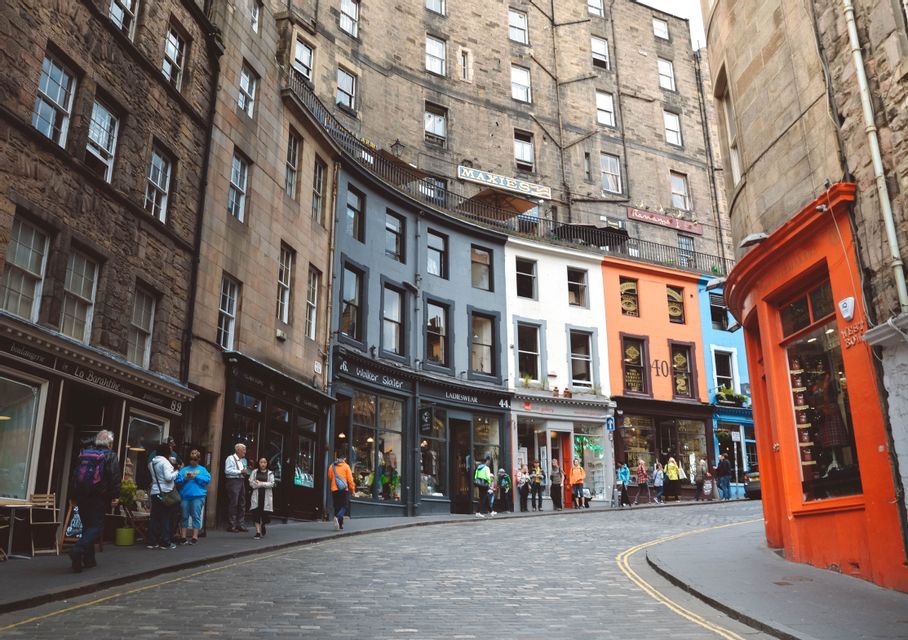 People walk along a curved cobblestone street lined with historic, colorful buildings and storefronts.