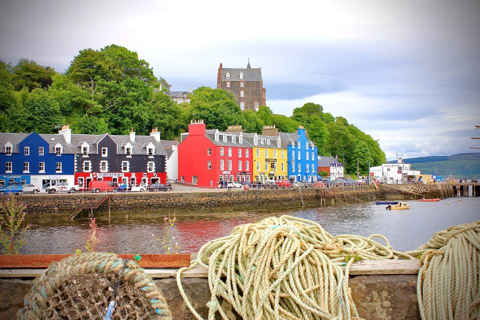 A row of brightly colored buildings lines a harbor waterfront, with thick nautical ropes coiled on a dock in the foreground.