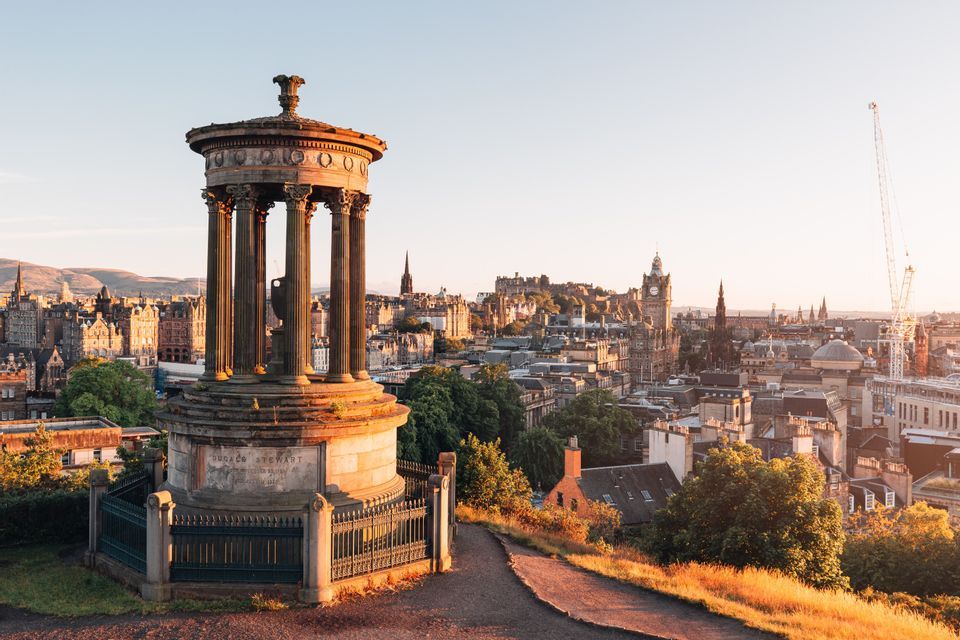 A classical monument with columns on a hill overlooking a historic cityscape bathed in golden sunset light.