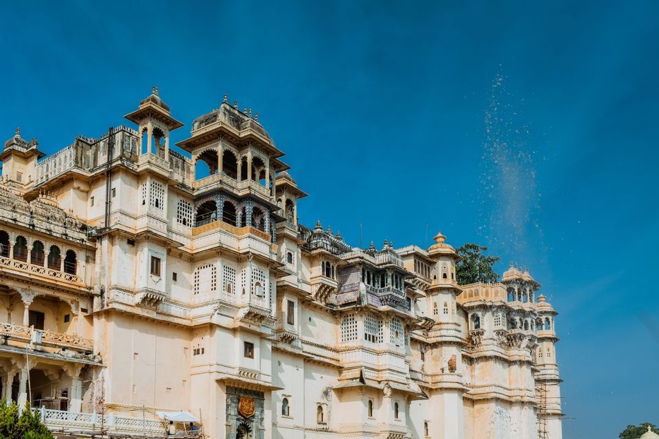 Un palazzo bianco, sontuoso e a più livelli, con torri e balconi intricati, si erge contro un cielo limpido e azzurro intenso.
