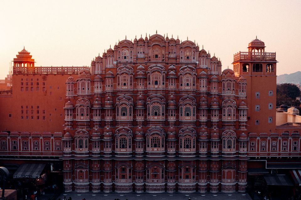 La fachada simétrica de un edificio de arenisca rojiza y ornamentada, con cientos de pequeñas ventanas y balcones bajo un cielo pálido al atardecer.