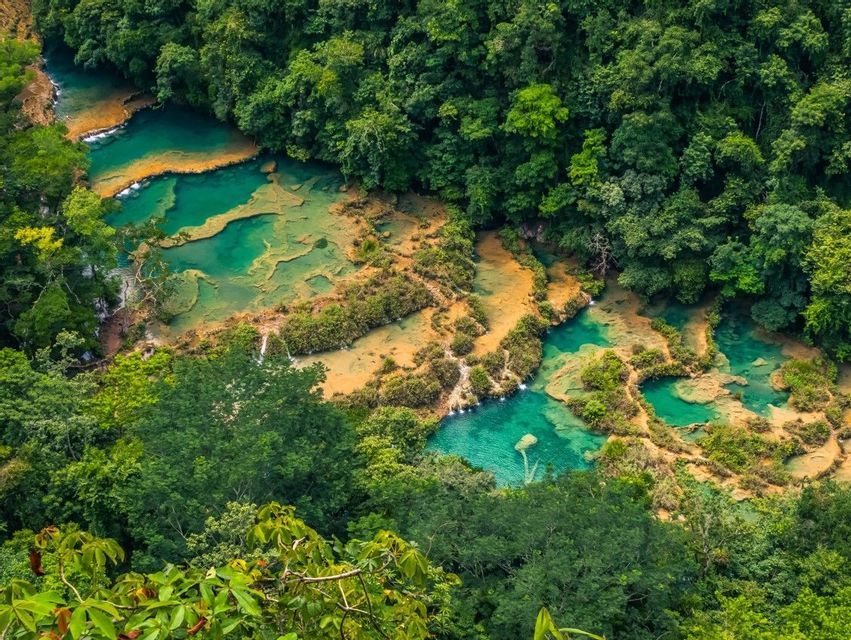Vista dall'alto di vivaci pozze d'acqua turchese che digradano a cascata su terrazze di calcare, immerse in una giungla rigogliosa e fitta.