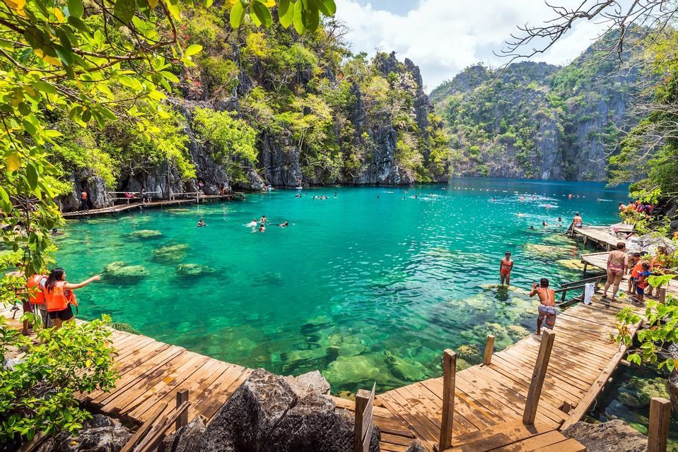 Un viaje en grupo de WeRoad nadando en una laguna turquesa cristalina, rodeada de acantilados rocosos con vegetación exuberante y pasarelas de madera.