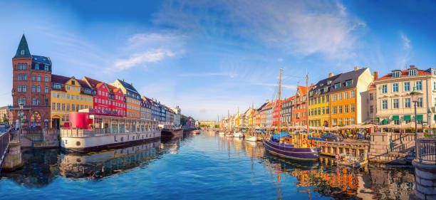 Una vista panoramica di un canale cittadino fiancheggiato da edifici colorati e barche ormeggiate sotto un cielo soleggiato e blu.