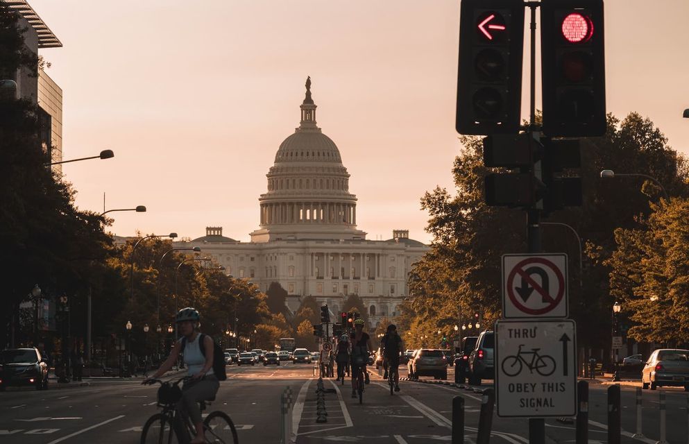 Radfahrer fahren eine Stadtstraße entlang mit dem US-Kapitolgebäude im Hintergrund während eines goldenen Sonnenuntergangs.
