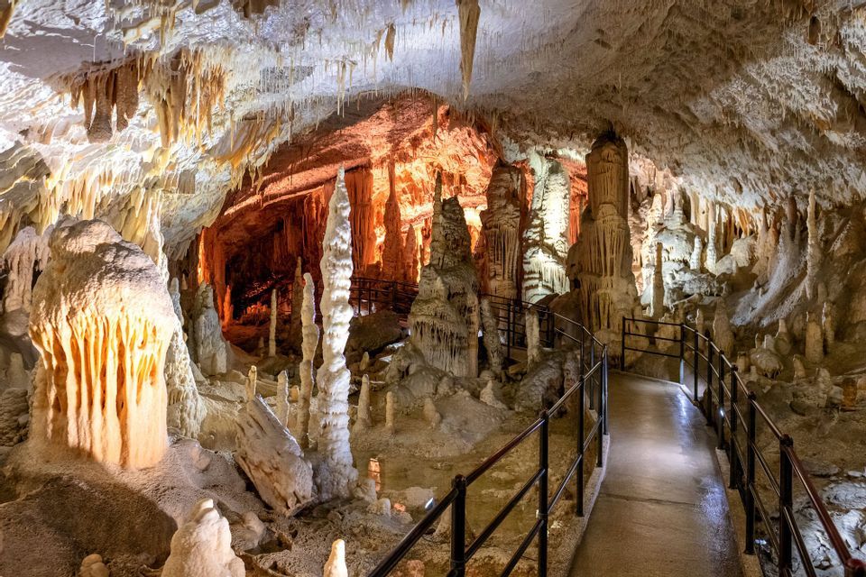 Un sentiero pavimentato si snoda attraverso una grande grotta piena di stalattiti e stalagmiti illuminate.