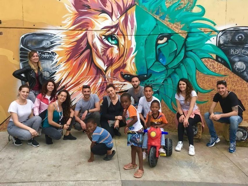 Un voyage de groupe WeRoad et trois enfants posant pour une photo de groupe devant une fresque colorée représentant un visage de lion.