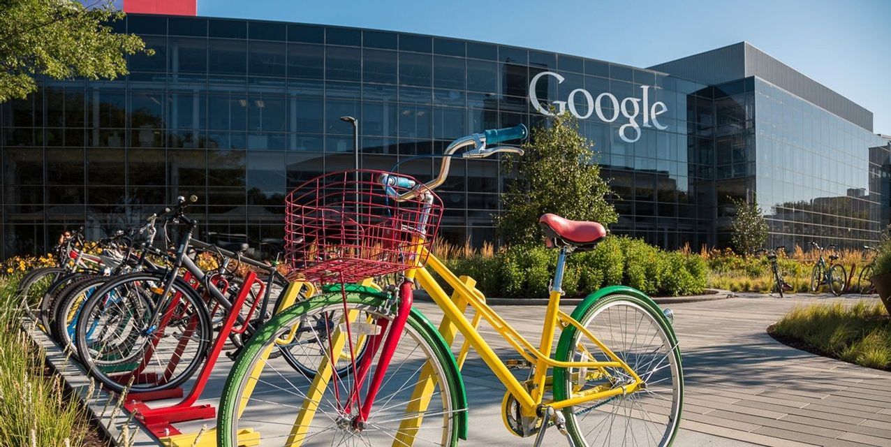 Biciclette colorate parcheggiate in una rastrelliera davanti alla moderna sede in vetro di Google in una giornata di sole.