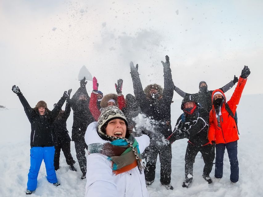 Una donna si scatta un selfie con il suo gruppo di viaggio WeRoad mentre festeggiano e lanciano neve in un vasto paesaggio innevato.