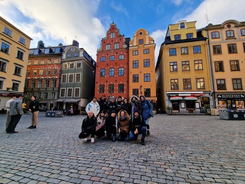 A WeRoad group trip poses for a photo in a cobblestone square in front of colorful historic buildings.