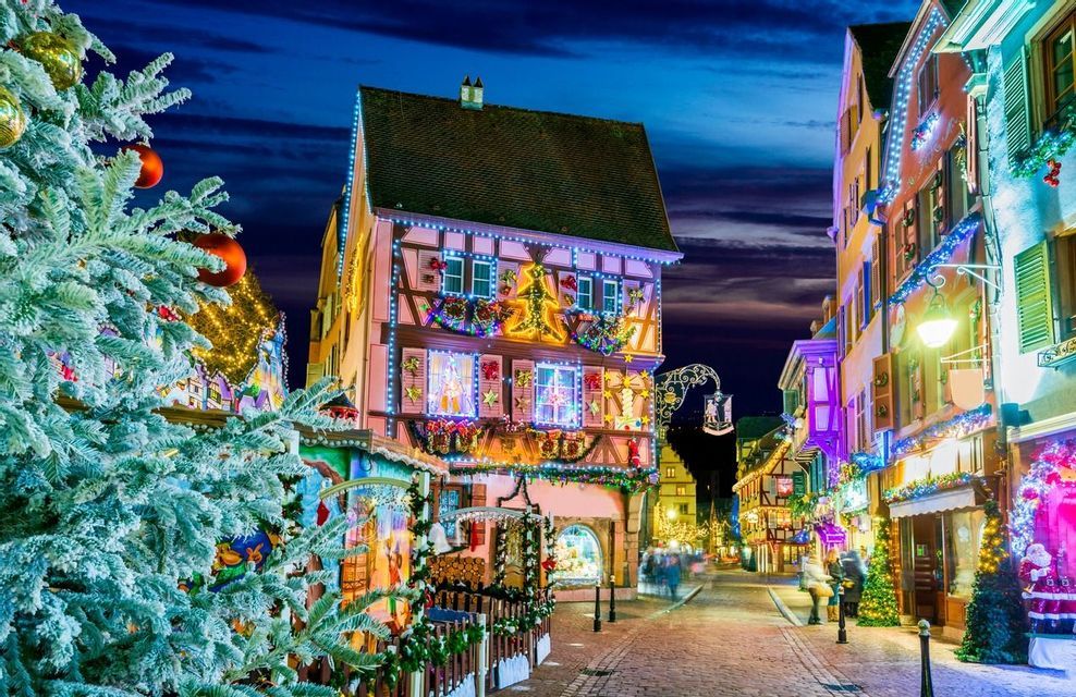 Una strada acciottolata con edifici a graticcio illuminati a festa con luci e ghirlande natalizie di notte.