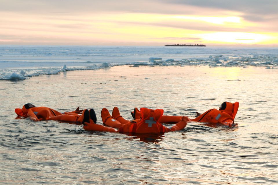 Un grupo de WeRoad flotando de espaldas en agua helada al atardecer, con trajes de inmersión naranjas.