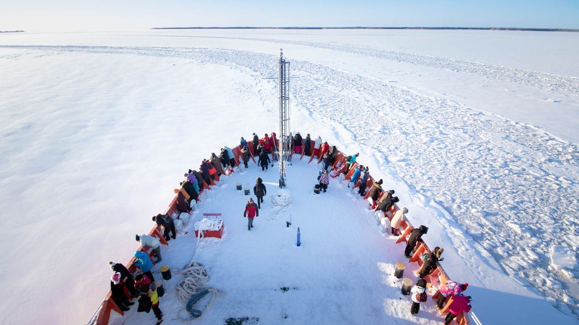 Un viaje en grupo de WeRoad de pie en la proa cubierta de nieve de un rompehielos, navegando por un vasto mar congelado.