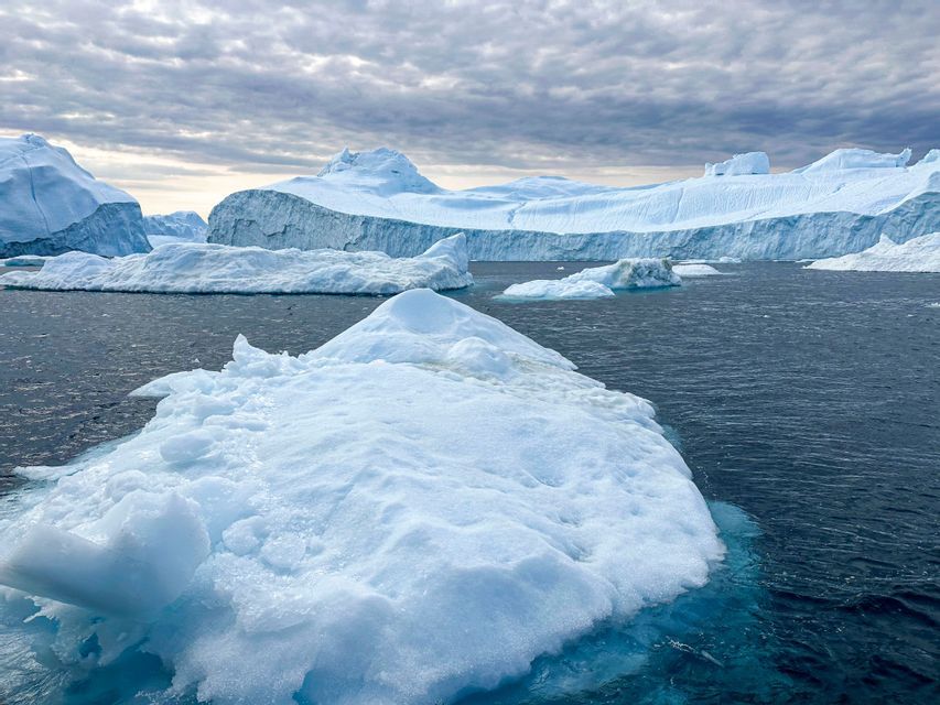 Grandi iceberg e ghiacciai che galleggiano in acque scure sotto un cielo nuvoloso.