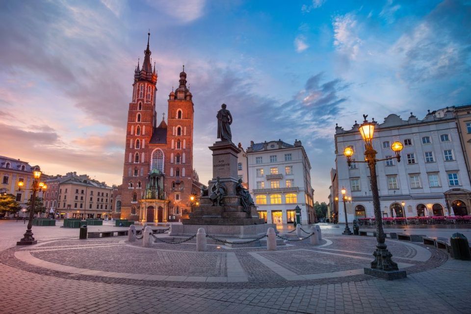 Una grande piazza acciottolata con una statua e una storica chiesa in mattoni illuminata dai lampioni al tramonto.