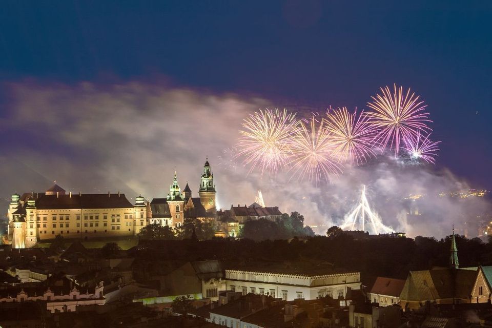Fuochi d'artificio su un castello illuminato e lo skyline della città di notte.