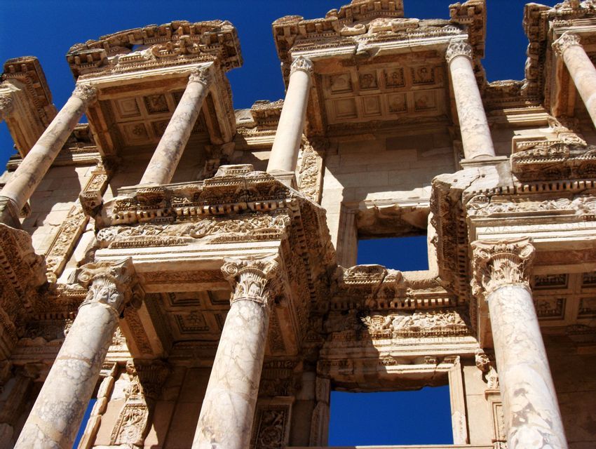 Una vista en ángulo bajo de la ornamentada fachada de piedra de una antigua ruina con columnas, contra un cielo azul profundo.
