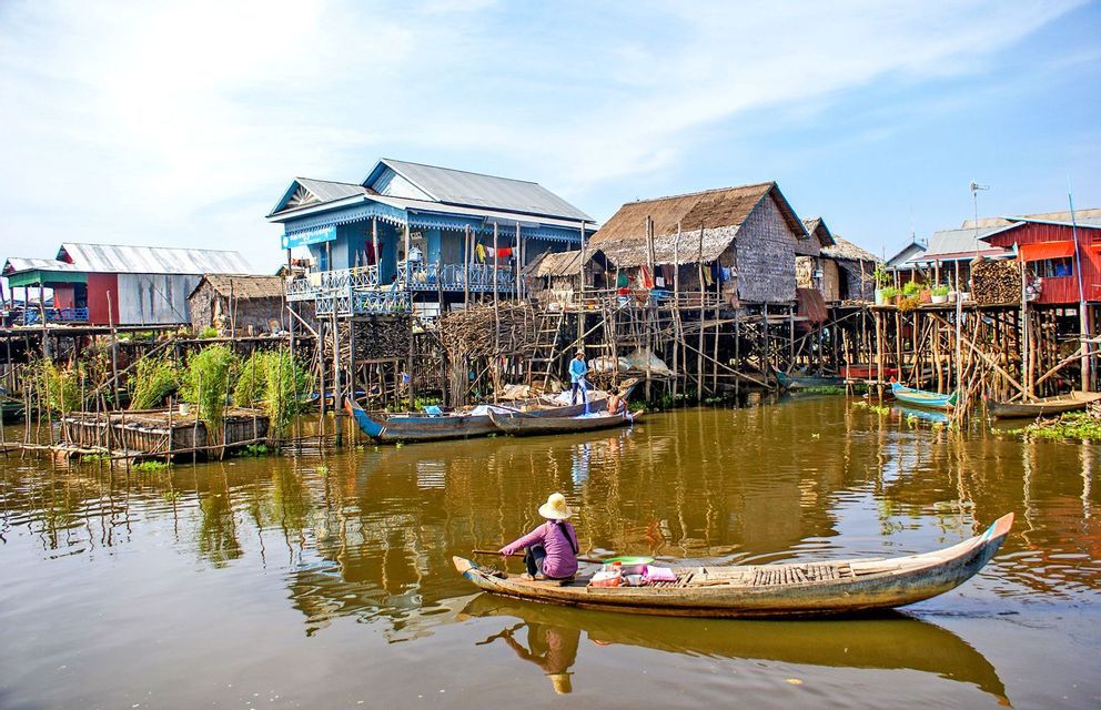 A person in a small boat paddles through a village of colorful houses built on stilts over the water.