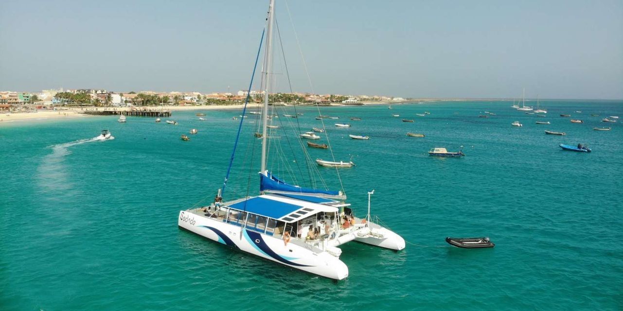 Un viaggio di gruppo WeRoad a bordo di un catamarano su acque turchesi, con una località costiera e altre imbarcazioni sullo sfondo.