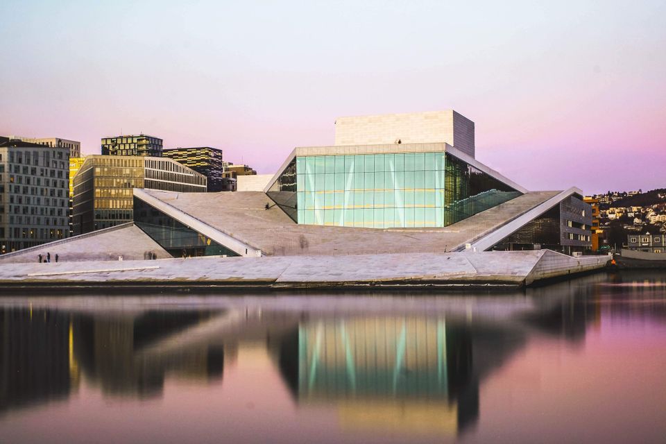Un moderno edificio architettonico con facciata in vetro si riflette in acque calme sullo skyline di una città al tramonto.