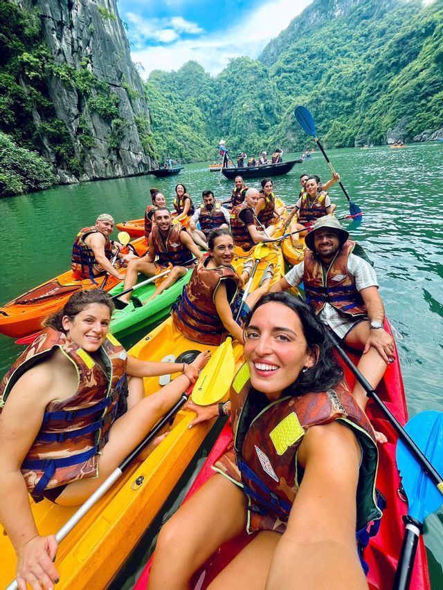 Un gruppo WeRoad, con giubbotti di salvataggio, sorride per una foto mentre fa kayak sull'acqua, circondato da ripide scogliere verdi.