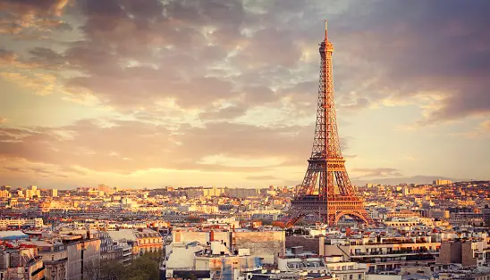 Ampia vista della Torre Eiffel e dello skyline circostante durante un tramonto dorato con nuvole sparse.