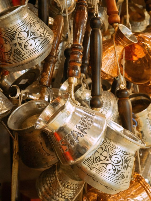 Una collezione di caffettiere turche incise e metalliche con manici in legno appese vicine, una con 'Istanbul' inciso sul lato.