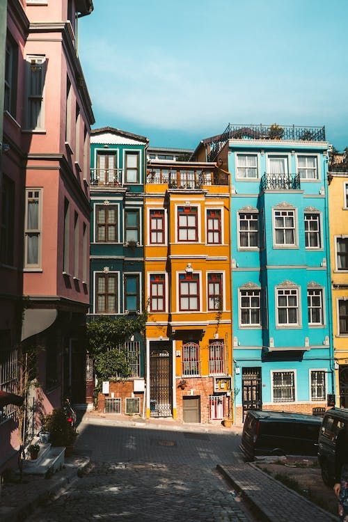 Una stretta via acciottolata è fiancheggiata da alti edifici colorati dipinti di rosa, verde acqua, giallo e blu.