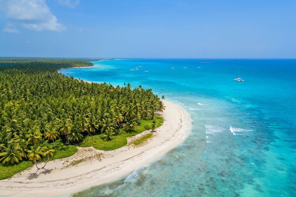 Veduta aerea di una spiaggia tropicale di sabbia bianca fiancheggiata da palme accanto a un oceano turchese con barche.