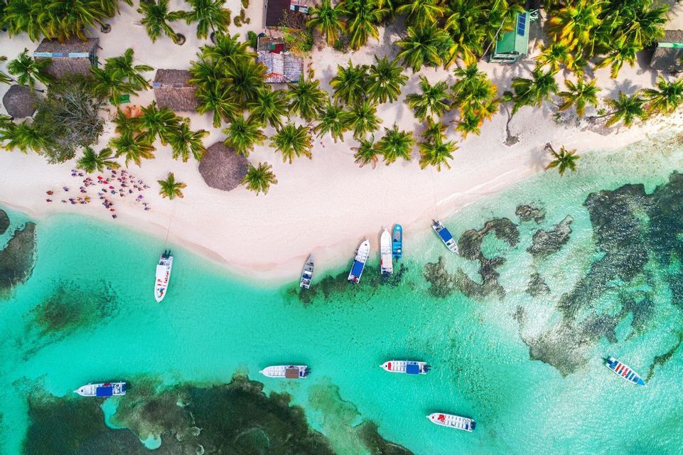 Una vista aerea di un viaggio di gruppo WeRoad su una spiaggia di sabbia bianca, con barche ormeggiate nell'acqua cristallina color turchese e circondata da palme.