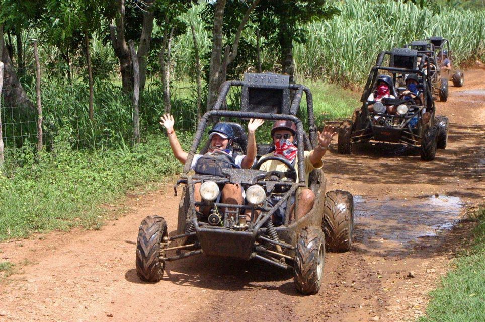 Due persone in un viaggio di gruppo WeRoad salutano dalla parte anteriore di un dune buggy fangoso, alla guida di un convoglio lungo un sentiero sterrato.