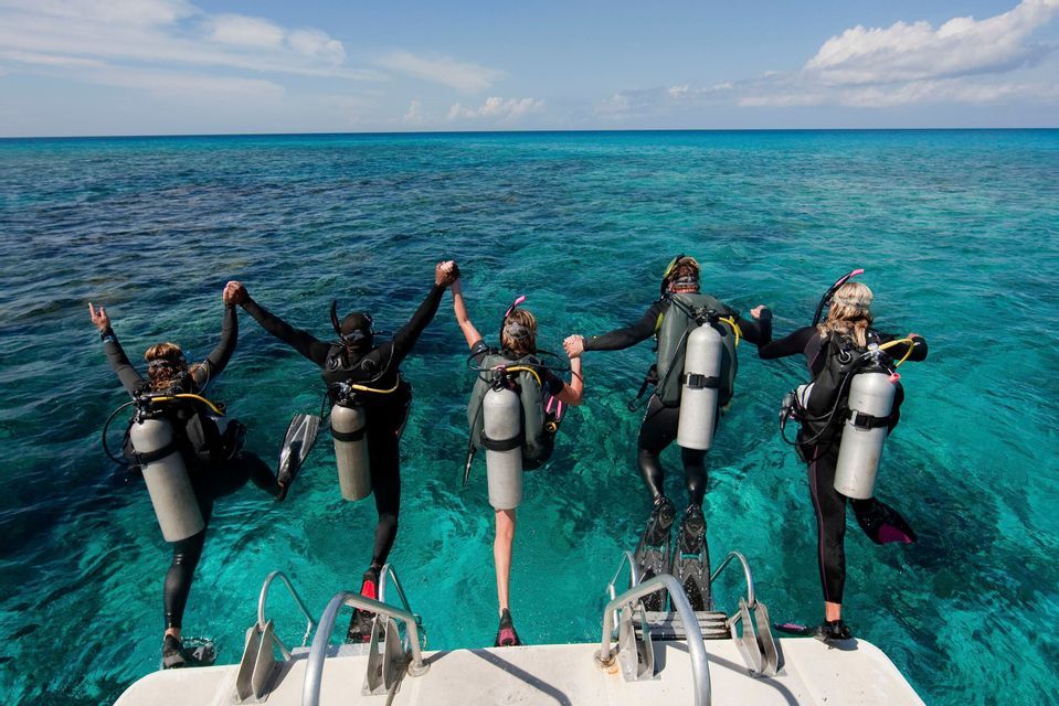 Un viaggio di gruppo WeRoad di cinque subacquei in muta che si tengono per mano mentre si tuffano da una barca in acqua turchese.