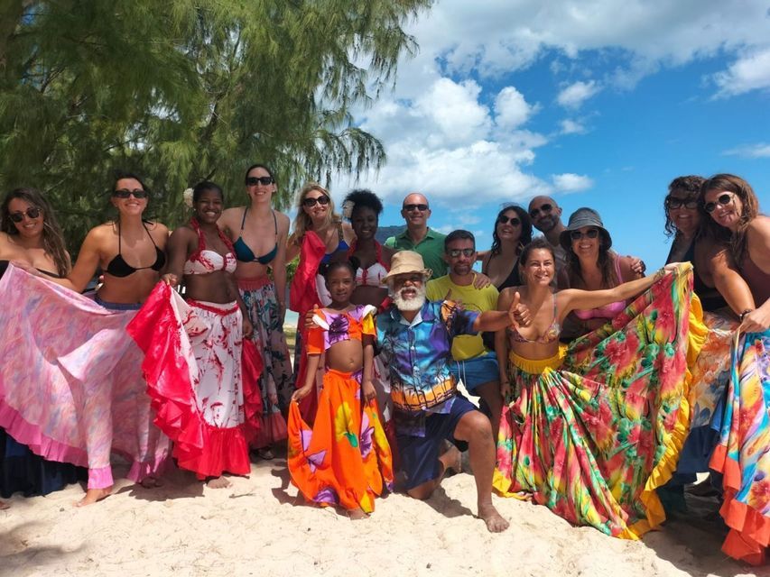 Un viaggio di gruppo WeRoad in posa con gente del posto che indossa abiti colorati su una spiaggia sabbiosa sotto un cielo azzurro.