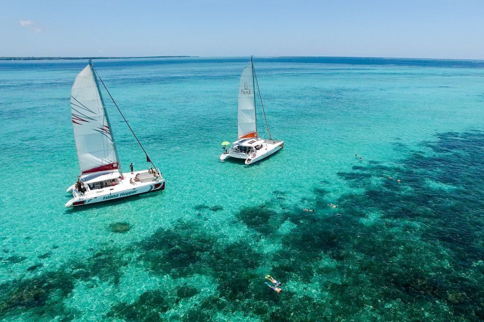 Una vista aerea di due catamarani con un viaggio di gruppo WeRoad che naviga su acque limpide color turchese, con persone che fanno snorkeling su una barriera corallina.