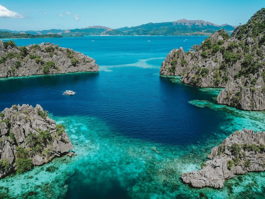 Vista aerea di una barca che naviga in una laguna turchese affiancata da grandi formazioni rocciose coperte dalla giungla.