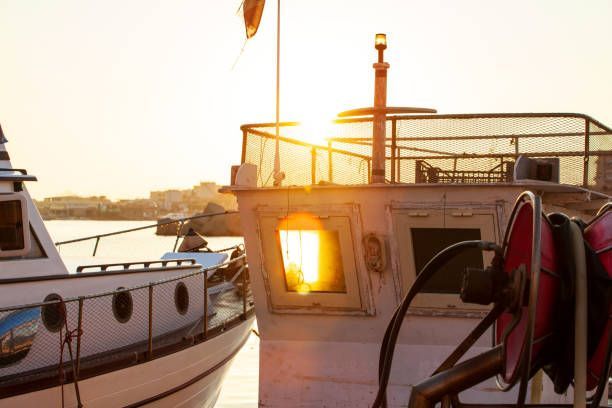 Due pescherecci sono ormeggiati in un porto al tramonto, con il sole che filtra attraverso il finestrino di una cabina.