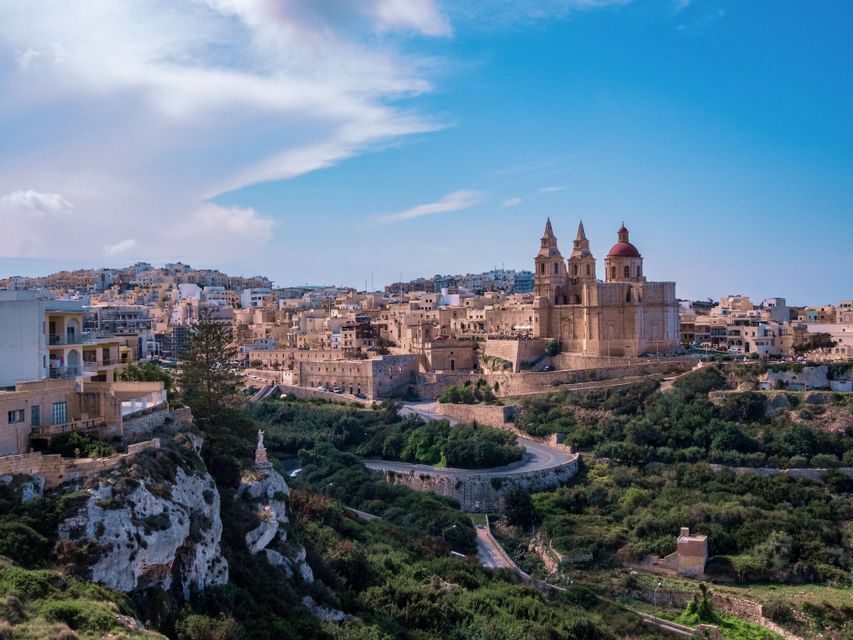 Una vista panoramica di una città storica su una collina, con una grande cattedrale dalla cupola rossa che domina una valle rigogliosa e verde.