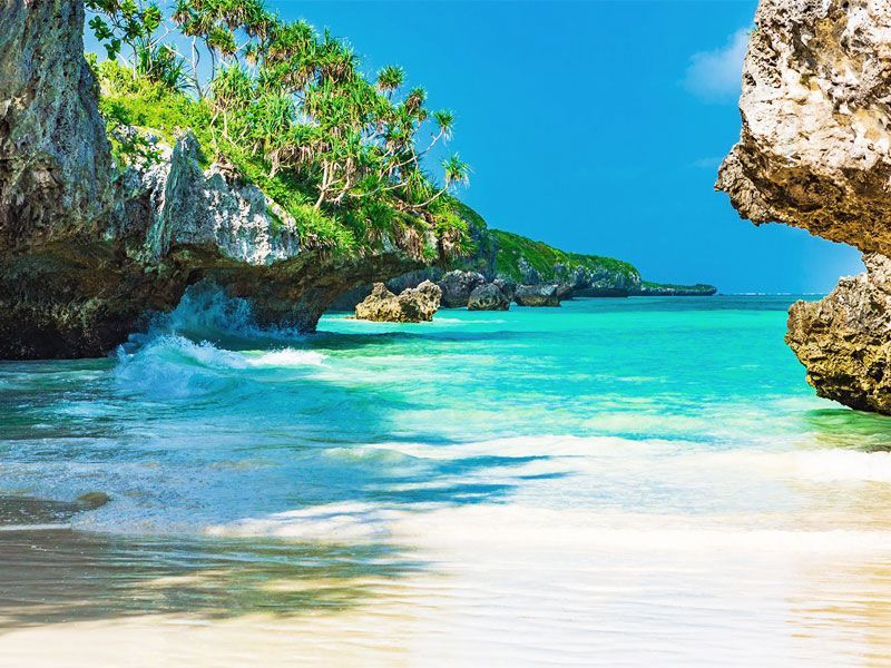 Una spiaggia tropicale con acqua turchese che lambisce sabbia bianca, incorniciata da scogliere rocciose coperte da vegetazione lussureggiante.