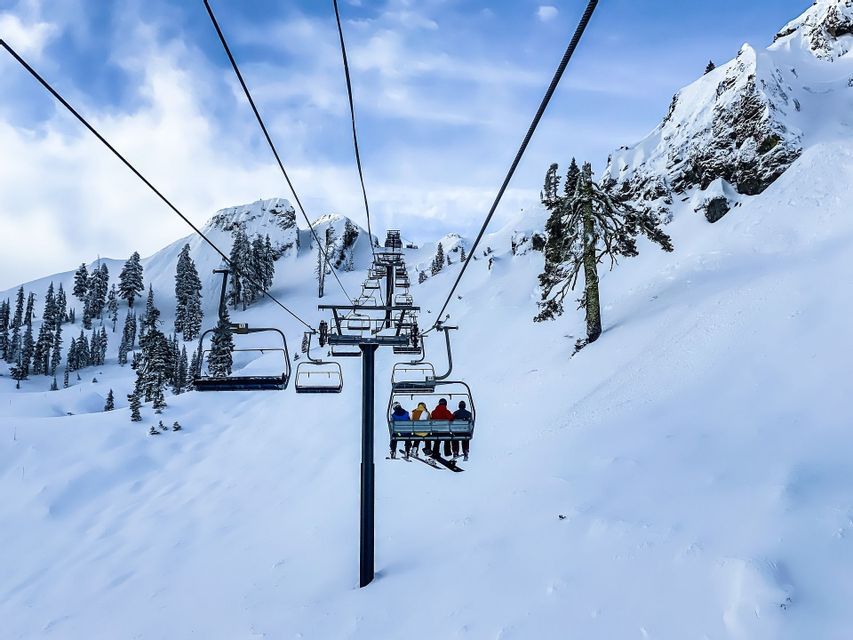 Un viaggio di gruppo WeRoad in seggiovia su un pendio montano innevato con alberi sempreverdi sotto un cielo parzialmente nuvoloso.