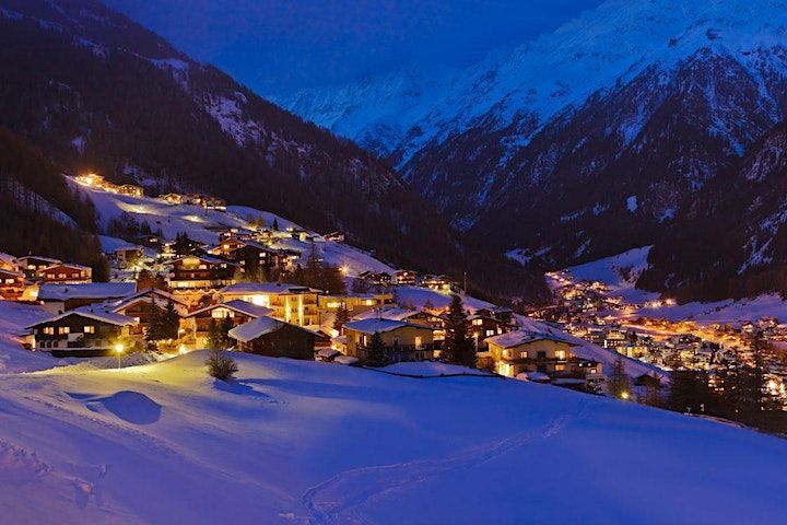 Un villaggio di case illuminate adagiato in una valle montana innevata al tramonto.