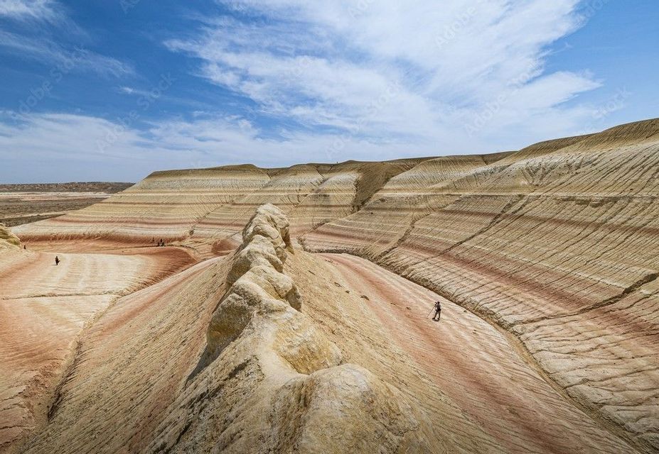 A WeRoad group trip hiking through a vast landscape of colorful, striped hills under a partly cloudy sky.