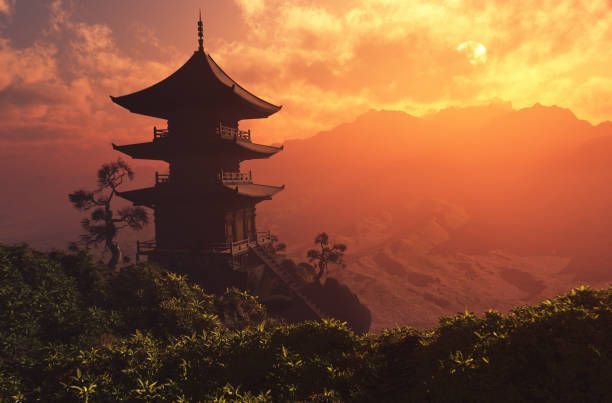 Un tempio pagoda in silhouette si erge su una collina rigogliosa che domina le montagne durante un tramonto arancione vibrante.