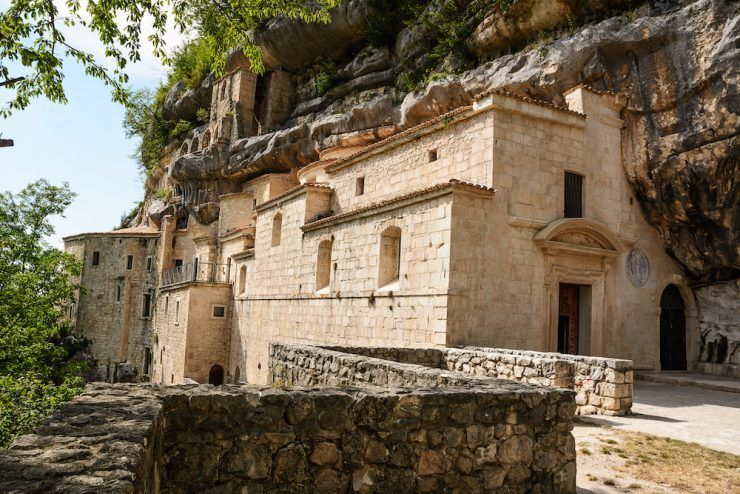 Un antico monastero in pietra costruito a lato di una ripida parete rocciosa, con alberi verdi che crescono sopra.