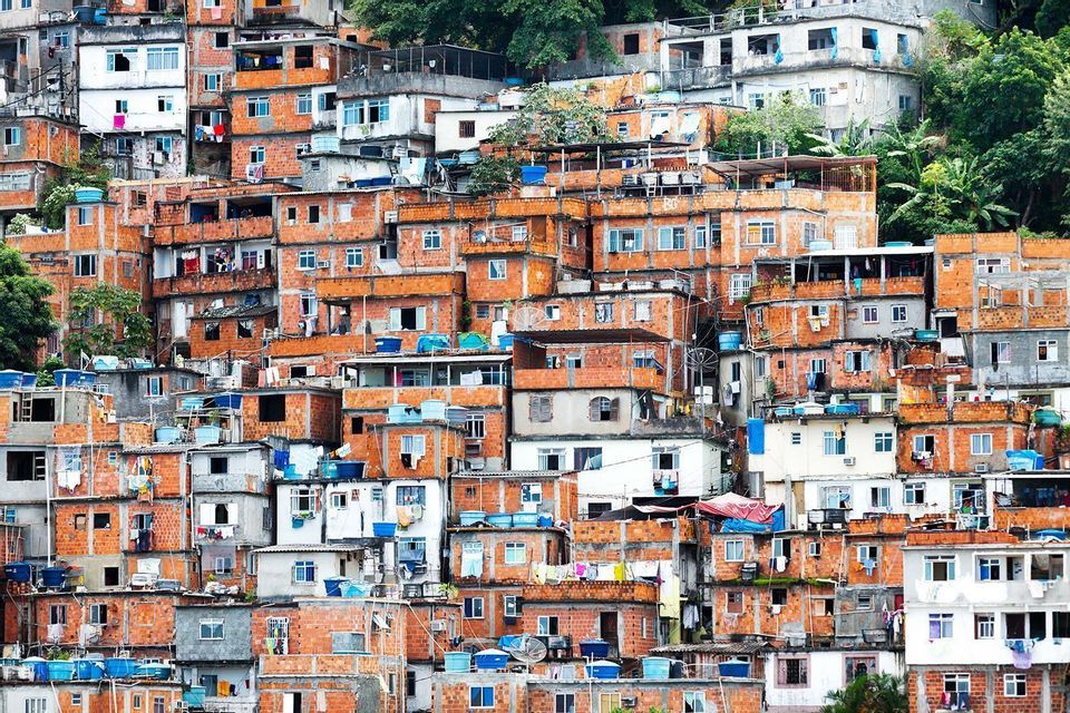 Densely packed red-brick and white buildings of a favela covering a green hillside.