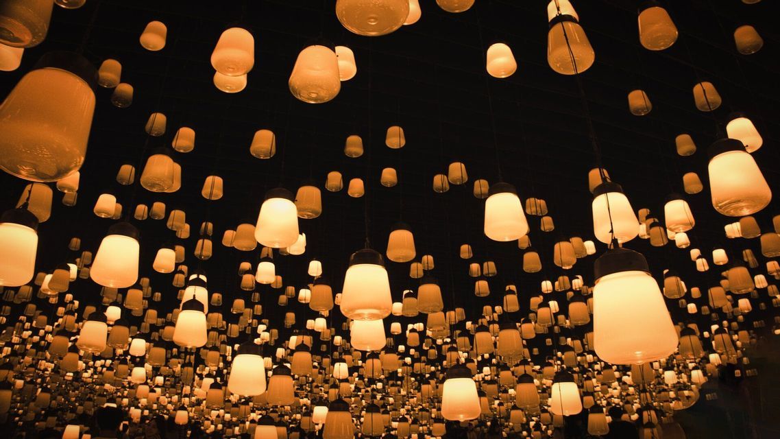 Una vista dal basso di innumerevoli lanterne arancioni luminose di varie dimensioni appese al soffitto in un ambiente buio.