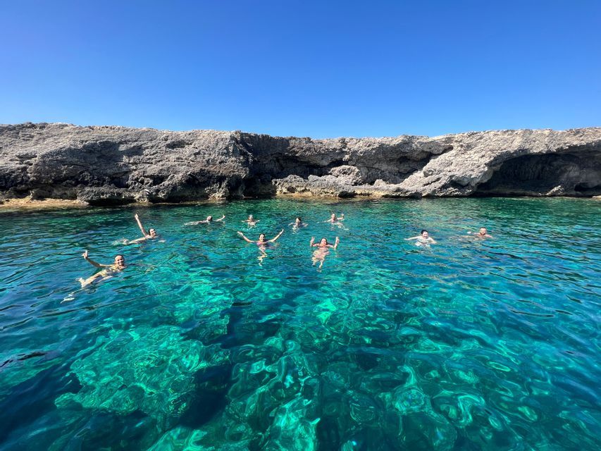 Un viaggio di gruppo WeRoad che si immerge in acque cristalline turchesi, vicino a una scogliera rocciosa, sotto un cielo azzurro brillante.