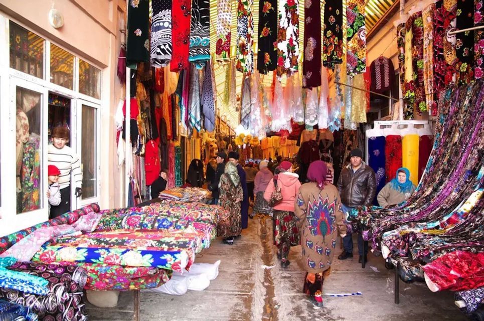 Le persone camminano attraverso un vivace mercato coperto pieno di bancarelle di tessuti colorati a fantasia e tessuti appesi.